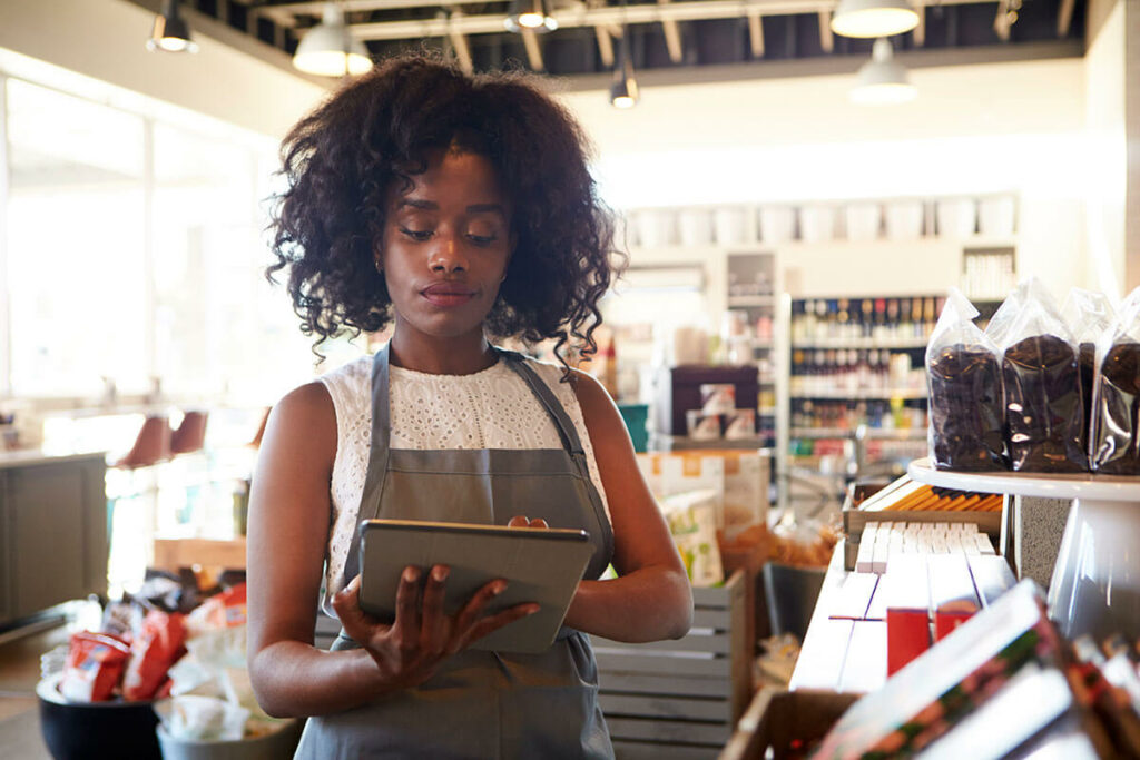 mulher negra de cabelos na altura dos ombros está fazendo a gestão de estoque de um mercado em um tablet
