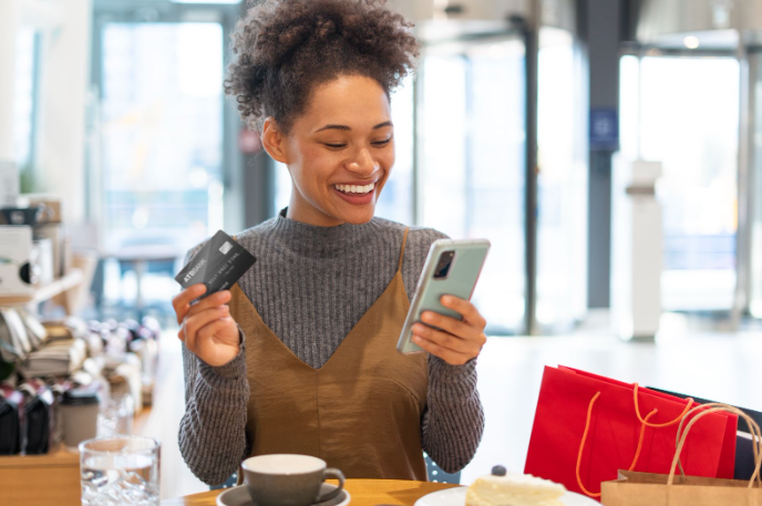 Mulher negra segurando um celular e um cartão de crédito simbolizando uma pessoa que faz parte de um programa de vantagens.