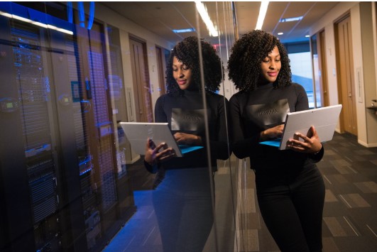 Mulher negra em ambiente corporativo com notenook nas mãos.